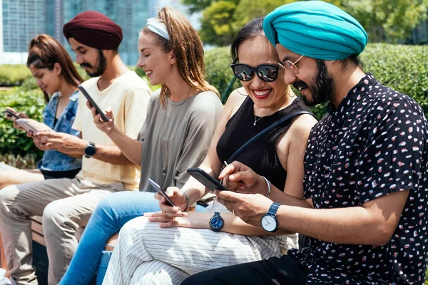 Group of multicultural friends using smartphone outdoors and having fun. Smiling people sitting outside and using mobile phone for social media, app, searching or typing message