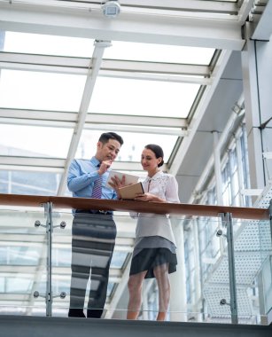 Toplantıdan önce strateji konuşacağız. Modern bir ofiste dikilirken dijital tablet üzerinde konuşan iki meslektaşın fotoğrafı.