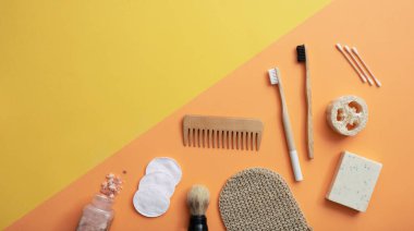 Tahta diş fırçaları, bambu kulak çubukları, lif süngeri, sağlam şampuan veya sabun, ahşap tarak, bez, banyo tuzu ve sarı ve turuncu arkaplanda fırça. Yeniden kullanılabilir sıfır atık plastik ücretsiz eko güzellik ürünleri