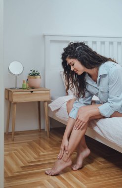 Gülümseyen kadın yatak odasında bacaklarına nemlendirici krem sürüyor.