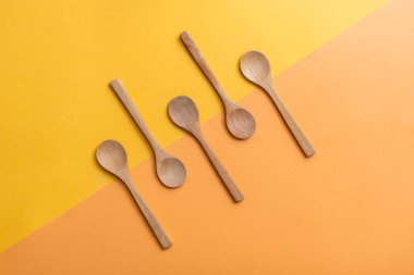 Geometrik arka plan grubunda tahta kaşıklar turuncu ve sarı arka planda beş boş tahta kaşık, fotokopi alanı ile üst manzara. Sıfır atık, bambudan yapılmış çevre dostu mutfak aletleri, sürdürülebilir yaşam tarzı konsepti