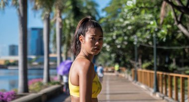 Güneşli bir günde parkta koştuktan sonra yorgun bir kadın kameraya bakıyor.