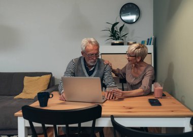 Son sınıf çifti evde dizüstü bilgisayarla online alışveriş yapıyor. Üst düzey bir adam dizüstü bilgisayar kullanıyor ve yaşlı bir kadın kredi kartı tutuyor. Çevrimiçi alışveriş, e-ticaret, internet bankacılığı, harcama, faturalar