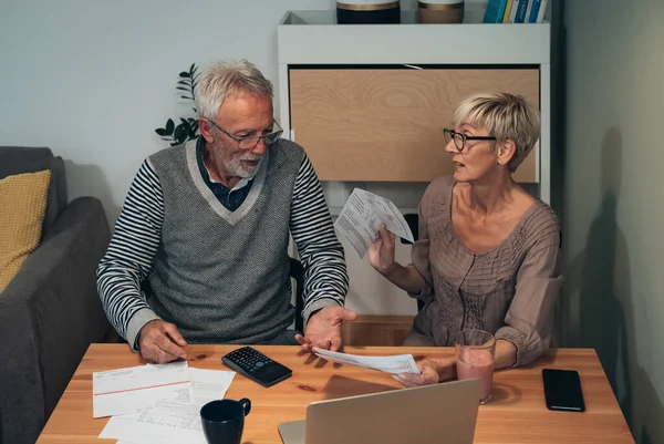 Senior couple fighting over money and expenses, angry couple arguing over domestic bills. Mature couple doing finance and having a hard time at home, calculating incoming bills and debt together and paying online on laptop computer