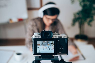 E-öğrenim sınıfları için internet üzerinden video kaydı yapan öğretmen. İnternette canlı yayın yapmak için kamera ve kulaklık kullanan kadın profesör, masa başında otururken kadınların el yazısını kaydeden kadın ellerine odaklan.