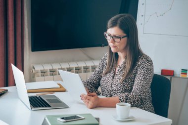 Dijital tablet işkadını üzerinde çalışan gülümseyen iş kadını, ofis masasındaki dizüstü bilgisayar ekranının önünde çalışırken evden işe giderken tablet kullanıyor.