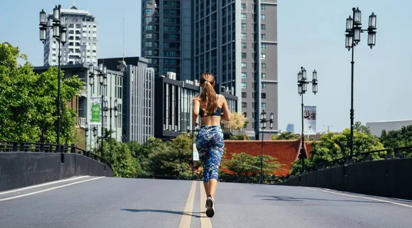 Rear view of woman running on city road with buildings in background. Back view of jogging woman in city street