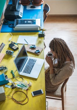 Kahve içen ve bilgisayar başında iş yapan bir kadın. Masada oturan bir kadın, evden çalışıyor ve elinde kahve tutuyor.