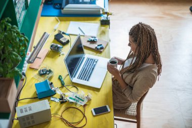 Kahve içen ve bilgisayar başında iş yapan bir kadın. Masada oturan bir kadın, evden çalışıyor ve elinde kahve tutuyor.