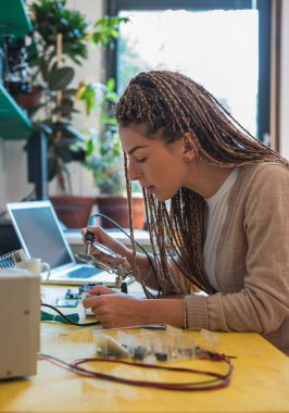 Kadın elektronik mühendisi atölyesinde lehimleme yapıyor. Elektronik tamir servisinde masa başında oturan ve ana kartı tamir eden genç bir kadın. Ev kavramından çalışmak