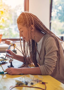 Kadın elektronik mühendisi masada otururken lehim yapıyor.