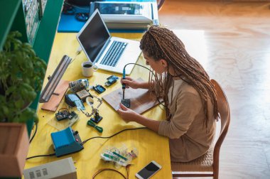 Kadın elektronik mühendisi atölyesinde lehimleme yapıyor. Nalbur tamirhanesinde kadın mühendis ya da teknik tamirci elektronik cihaz tamir ediyor.