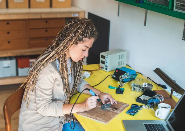 Woman soldering a circuit board in her tech office. IT technician soldering circuit board. Microchip production factory. Assembling the PCB board. Technological process
