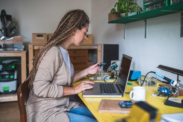 Female engineer working on laptop computer. Woman engineer siting at desk using laptop computer, holding and lookin circuit board