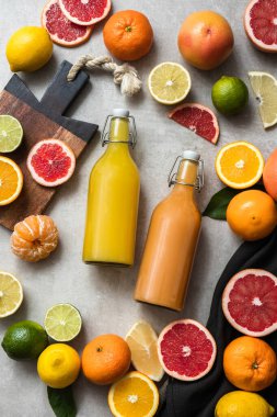 Şişelerde taze sıkılmış narenciye suyu ve beton mutfak masasında taze meyveler. İki cam şişe taze greyfurt suyu ve portakal suyu, tahta kesme ve beton masa üzerinde taze meyveler. Sıfır atık, plastiksiz yaşam tarzı konsepti