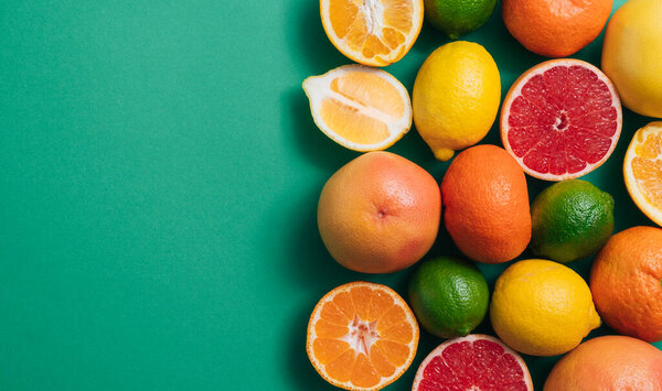 Citrus fruit on green table with copy space. Fresh citrus fruit including lime, lemons, orange, yellow grapefruit, pink grapefruit and tangerines on green background with empty space