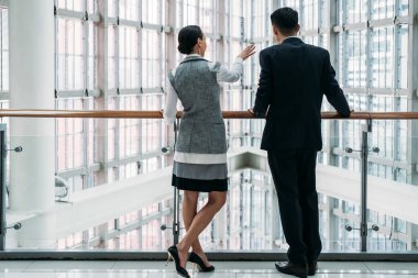 Modern koridor balkonunda duran ve iş hakkında konuşan iki iş arkadaşının arka görüntüsü.
