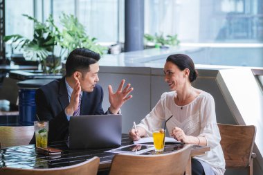 İş ortakları restoranda başarılı bir toplantı yapıyorlar. Konuşan ve gülümseyen iki kendine güvenen iş adamı takımı. İş adamı iş evraklarını tutuyor ve iş kadını dizüstü bilgisayar kullanıyor ve birlikte tartışıyorlar.