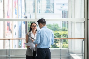 İş adamları ofise bakan pencerelerin önünde birlikte dijital tablet kullanıyorlar. Ortağına bakan gülümseyen iş kadını. İş planlama ve organizasyon, evrak işi kavramı
