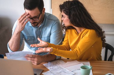 Genç mutsuz çift, ev masasında faturalar ve harcamalar hakkında tartışıyor.