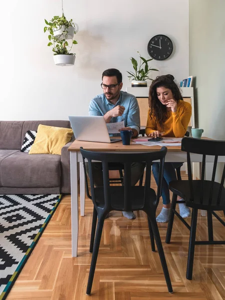 Serious couple calculating domestic bills together at home. Beautiful husband and wife sitting at desk and paying bills online from home