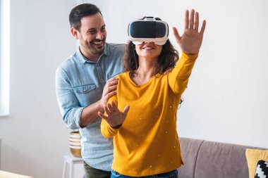 Kadın sanal gerçeklik deneyimi sırasında havaya dokunuyor. Genç mutlu çift sanal gerçeklik kulaklığıyla eğleniyor.