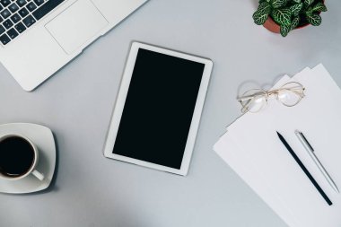 Bilgisayarlı gri ofis masası, dijital tablet, bir fincan kahve ve diğer malzemeler. Çalışma masasının en üst görüntüsü, ev konseptinden çalışıyor