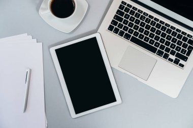 Gri masadaki ofis malzemelerinin en üst görüntüsü. Bilgisayarlı, tabletli, kahveli, kağıtlı ve kalemli bir iş masası. Evden çalışmak, ofis kavramı.