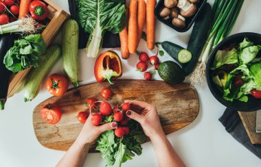Kadın ellerinin organik sebzelerle dolu masada taze salata yaptığı masa manzarası. Ev hanımlarının evde taze sebzelerle öğle yemeği yediği fotoğrafın hemen üstünde. Vejetaryen yemeği veya vejetaryen yemeği, sağlıklı beslenme konsepti.