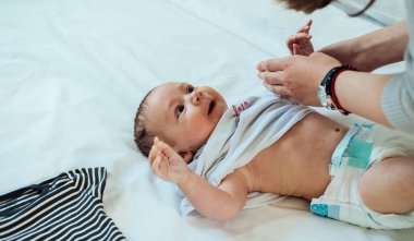 Anne Küçük Bebeği Yatakta Giydiriyor. Yatakta yatan ve annesi tarafından giydirilen sevimli bir bebeğin fotoğrafını çek..
