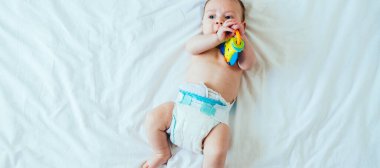 Sevimli Bebek Portresi Yatakta Taklit Alanlı Çıngıraklı Çıngırakla Oynuyor. Bebek bezi içinde bebek bezinin üzerinde uzanan ve çıngıraklı oyuncak tutan bebek manzarası.. 