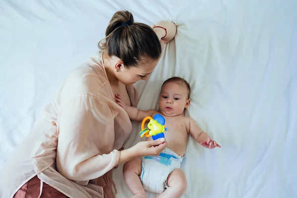 Νεαρή Μητέρα Κρατώντας Rattle Toy Και Ξαπλωμένη Στο Κρεβάτι Νεογέννητο — Φωτογραφία Αρχείου