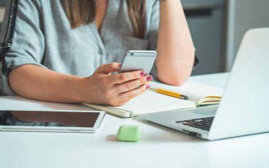 Tanımlanamayan İş Kadını Ara Veriyor ve Cep Telefonuyla Mesaj Gönderiyor veya Birilerini Ara. İş yerinin ofis masasında dizüstü bilgisayar, tablet, not defteri, kulaklık ve işten önce akıllı telefon tutarken çekilmiş fotoğrafı..