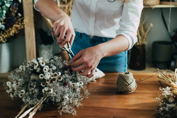 女性の花屋の手コピースペースで木製のテーブルでドライフラワーの永遠の花束を作る彼女のワークショップで乾燥した花や植物の花束を手配している認識できない女性起業家の写真を閉じます — ストック写真