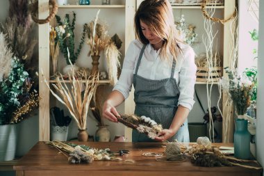 Atölyesinde Kuru Çiçeklerin Çiçeklerini Düzenleyen Güzel Çiçekçi. Stüdyosunda kurumuş bitki ve çiçeklerle sonsuz çelenk yapan yetenekli genç bir kadın. Sürdürülebilir yaşam tarzı konsepti..