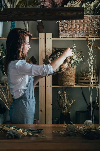 笑顔の花屋彼女のワークショップで乾燥した花の花輪を手配します 若い才能のある女性は 彼女のスタジオで乾燥した植物や花で永遠の花輪を作り 持続可能なライフスタイルコンセプト — ストック写真