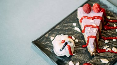 Sağlıklı bir dilim ahududu keki, içinde meyveler ve fındıklar bir kafede gri bir tabakta servis edilir.