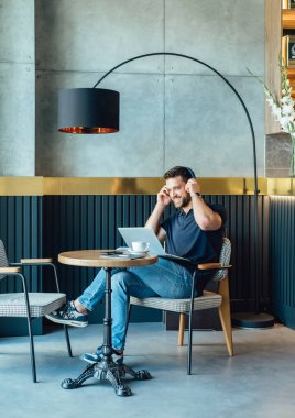 Handsome Businessman Putting Wireless Headphones Before Online Meeting in a Cafe.Cheerful smiling business man with headphones having conference call meeting online on laptop computer or listening to music from a restaurant.