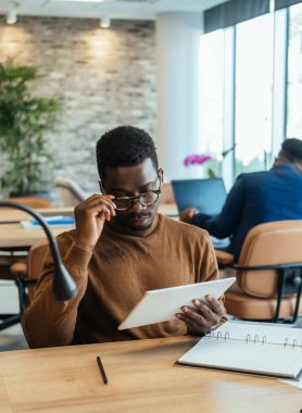 İş adamının İş Tabletindeki İş Grafiklerini Analiz Etmesi. Yakışıklı Afro-Amerikan işadamı, şirket açık iş planı ofisinde otururken iş raporlarını okumak için dijital tablet kullanıyor..