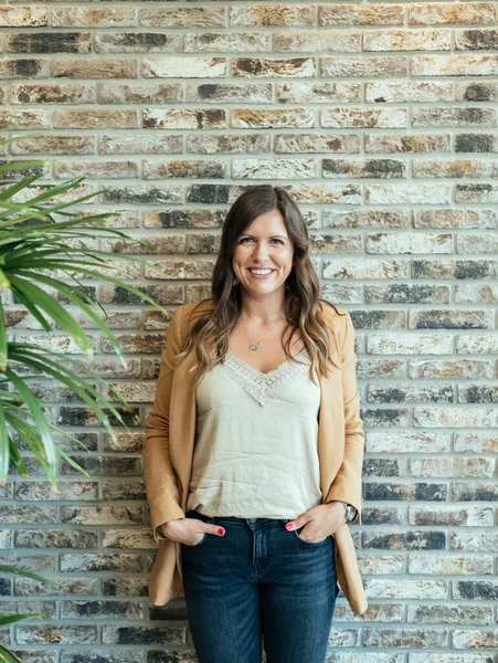 Portrait of Smiling Business Woman Standing Against the Brick Wall. Beautiful  cheerful casual businesswoman with hands in pocket standing against the brick wall and looking at camera.