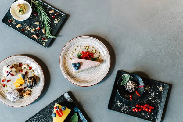 Top View of Table full with Different Protein Balls and Healthy Cakes.Directly above photo of sugar free desserts with fruits and nuts: few healthy energy balls and fruit cakes served on black plates in a restaurant table with copy space.