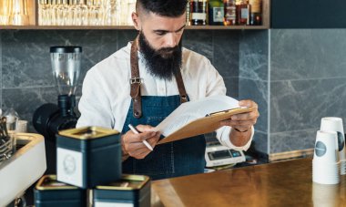 Yakışıklı Barista bir kafede ürünlerin envanterini yapıyor. Bar tezgahında sakallı, ciddi bir garson. Restoranda hisse senedi saymak için pano kullanıyor..