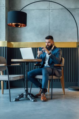 Cafe 'de dizüstü bilgisayar üzerinde çalışırken cep telefonu kullanan yakışıklı bir iş adamı. Ciddi bir iş adamı, sakallı, bir restoranda oturup çalışırken telefonla mesaj yazıyor..