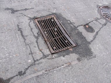 Kırık asfaltta paslı rögar ızgarası
