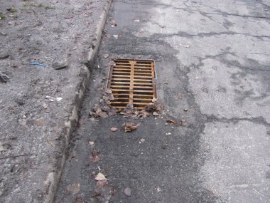 Kırık asfaltta paslı rögar ızgarası