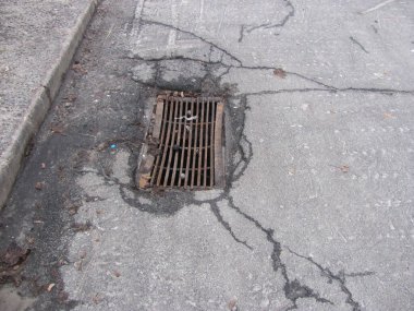 Kırık asfaltta paslı rögar ızgarası