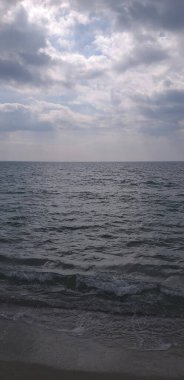 dikey arkaplan: dalgalar kıyıda yuvarlanıyor, bulutlu mavi gökyüzü