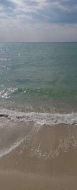 dikey arkaplan: dalgalar kıyıda yuvarlanıyor, bulutlu mavi gökyüzü