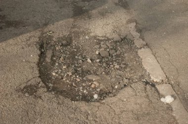 Asfalt yolda bir çukur var, yüzeyinde kavak kabarcıkları var, aşınma ve açık hava detaylarını gösteriyor..