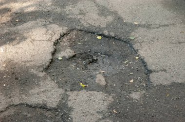 Eski, hasarlı bir yolda asfaltta bir çukur, aşınma ve çürümeyi gösteriyor..